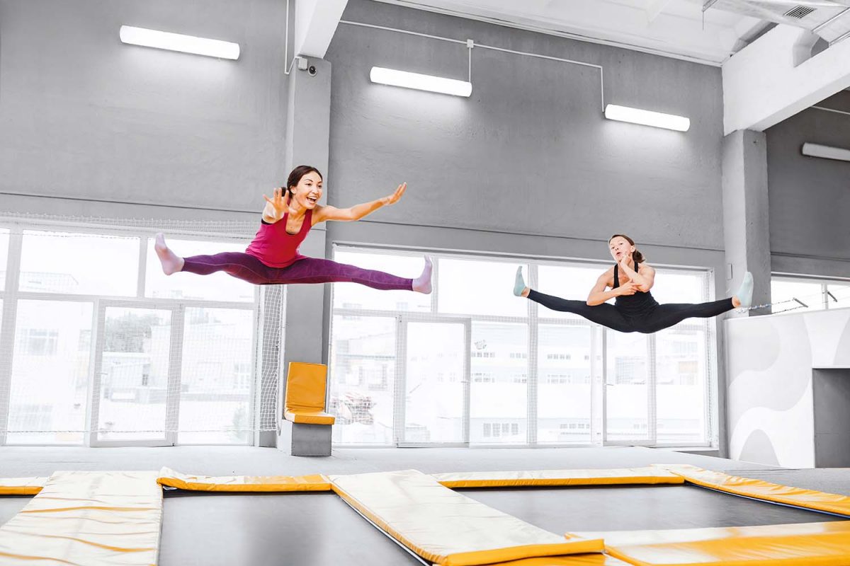Two young active women jumping on trampolines in a modern fitness center.